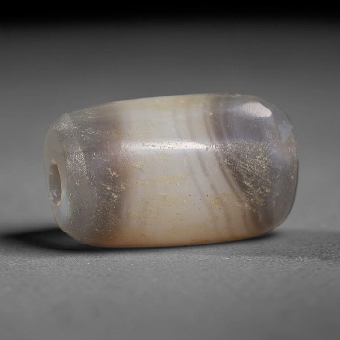 Ancient Agate Bead - Silk Road Miniature Amulet: Carved from banded agate, the bead features a short barrel form with a smooth, polished surface that highlights the stone's natural concentric banding, ranging from smoky gray and soft taupe to warm h