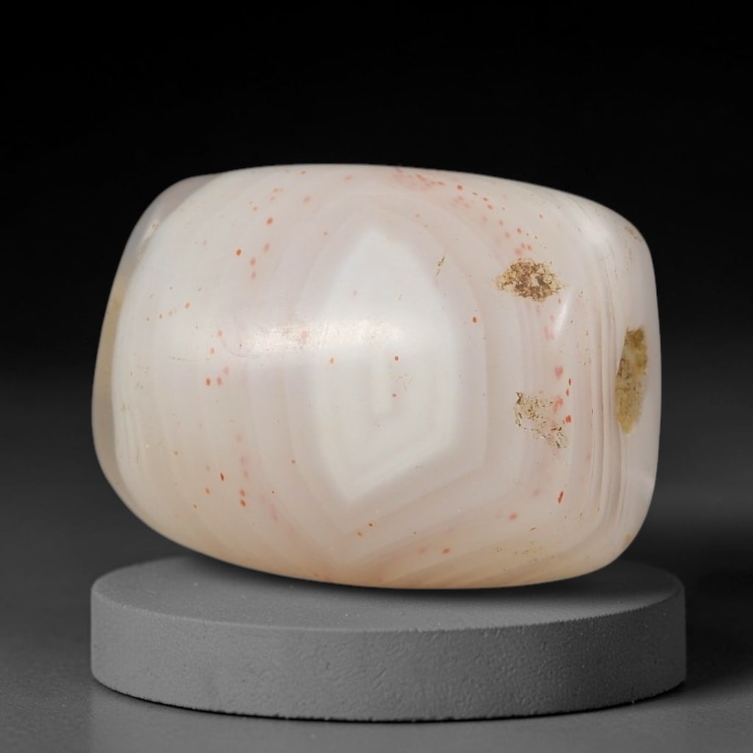 Ancient Agate Bead - Indus Valley Amulet: This artifact is crafted from pale creamy white agate, exhibiting a striking concentric "eye" banding pattern with scattered vivid red mineral inclusions, shaped into a smooth barrel form through skil