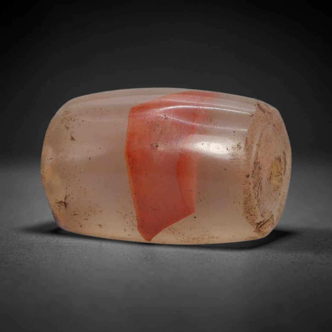 Ancient Agate Bead - Indus Valley Banded: This artifact is crafted from translucent agate, featuring a striking band of vivid reddish-orange contrasting with pale, creamy white base tones across its polished surface. The bead is formed in a s