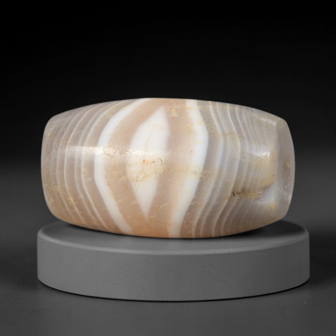 Ancient Banded Agate Bead - Near Eastern Artifact: This artifact is crafted from natural banded agate, shaped into a short barrel form with striking concentric banding in warm taupe and bright white, forming a central eye-like diamond pattern. The bea