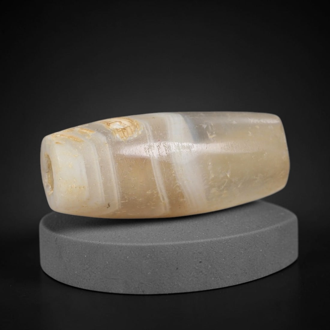 Ancient Banded Agate Bead - Near Eastern Artifact: This artifact is crafted from natural banded agate, shaped into an elongated, faceted barrel form with distinct concentric banding in warm taupe, cream, and amber hues. The bead features a central per