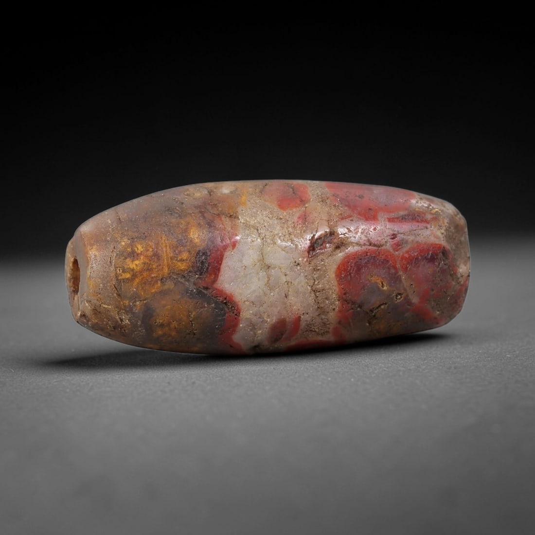 Ancient Agate Barrel Bead - Silk Road Indus Valley Bead: Carved from multicolored brecciated agate, the bead is fashioned in a compact barrel form, with a central drilled perforation for suspension. The stone exhibits striking natural inclusions in deep red