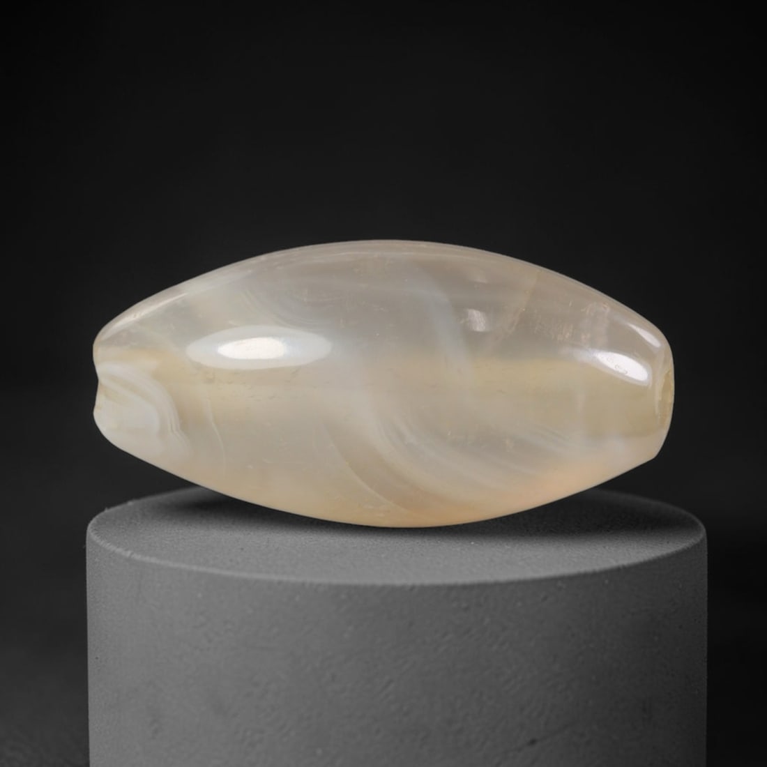 Ancient Agate Bead - Indus Valley Silk Road: Carved from banded agate, the bead is fashioned in a bi-conical barrel form with a central perforation for suspension. The stone displays natural, subtle concentric banding in creamy white and translu