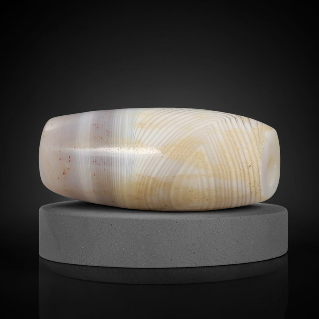 Ancient Agate Bead - Indus Valley Amulet: This artifact is crafted from banded agate, exhibiting fine concentric layered striations in creamy white, warm honey, and pale grey tones with subtle red mineral inclusions, shaped into a smooth barr