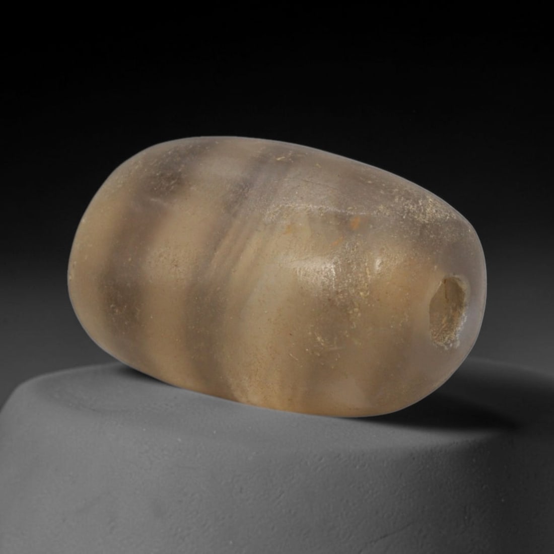 Ancient Agate Bead - Bactrian Banded Barrel Bead, 24XW: This bead is carved from translucent smoky-grey banded agate, shaped into a smooth, compact barrel form with a precisely centered axial drill hole, characteristic of ancient Bactrian lapidary craftsma