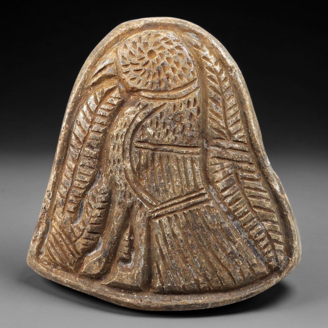 Ancient Stone Plaque Relief - Near Eastern Bird Figurine, 77BE: Carved from a single piece of stone, this bell-shaped relief plaque depicts a stylized bird, rendered in the linear, incised artistic tradition of the ancient Near East. The figure is detailed with a