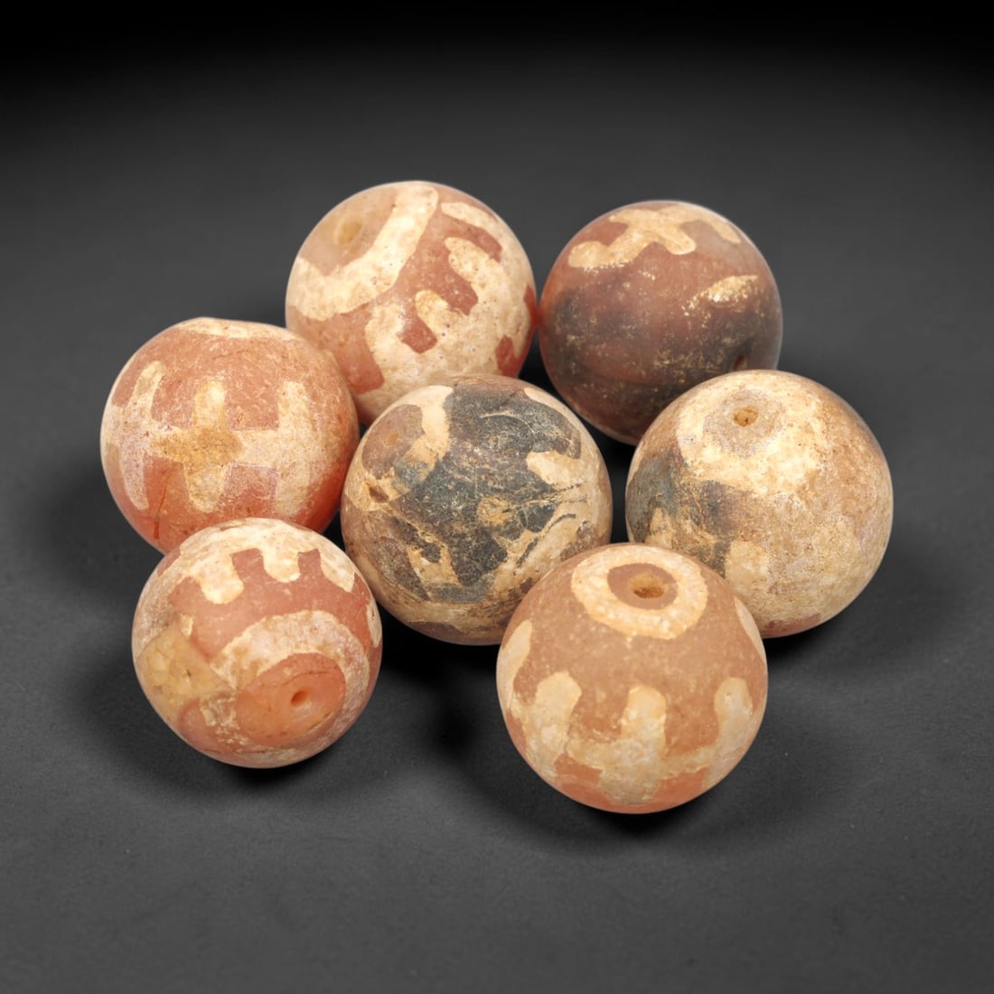 Ancient Carnelian Etched Beads - Gandhara Amulet Set, 68XY: Set of seven spherical beads crafted from carnelian, each decorated with etched geometric motifs in a pale white pigment, characteristic of Gandharan decorative traditions. The beads retain a well-dev