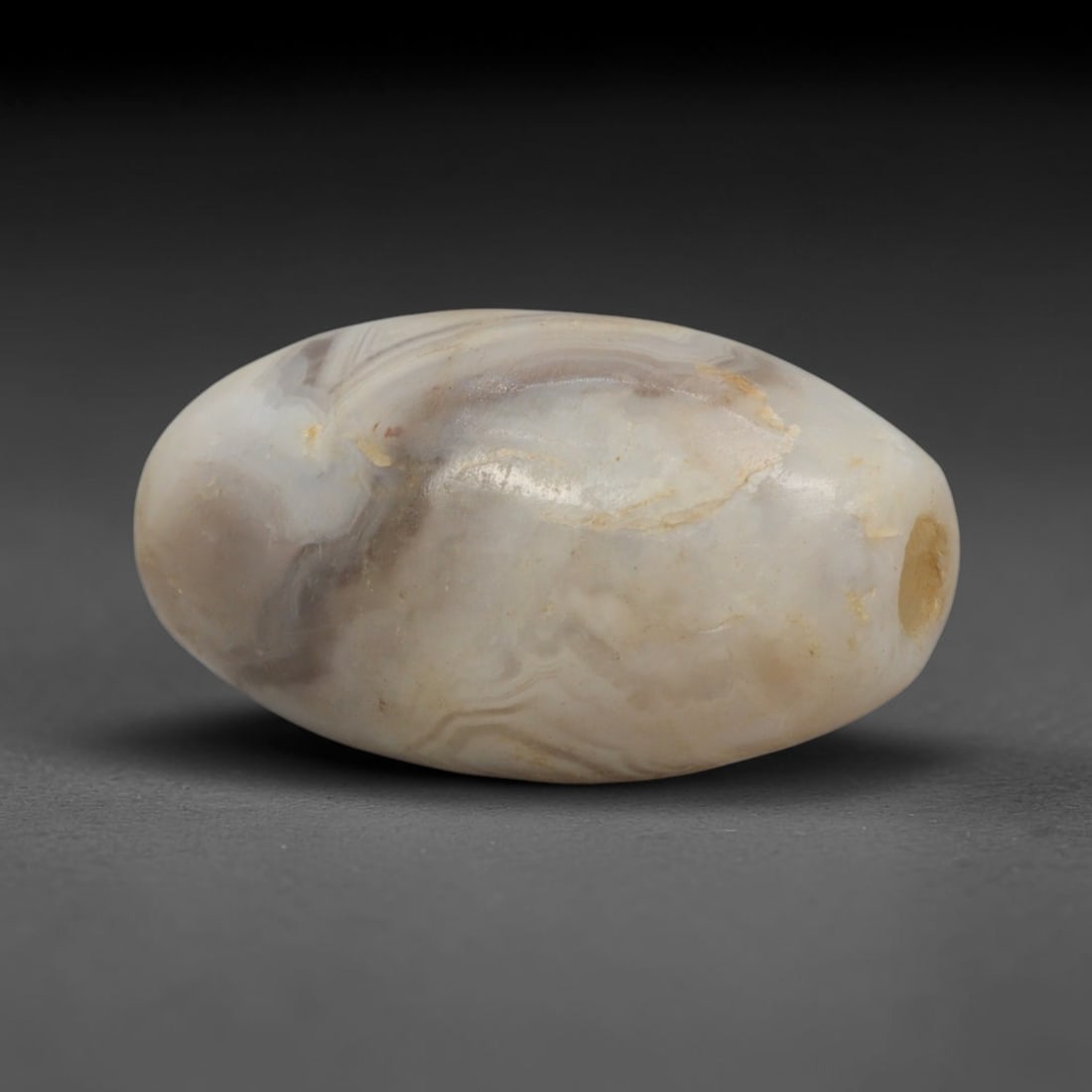 Ancient Agate Bead - Indus Valley Banded Oval Bead, 62XW: This bead is carved from translucent creamy-white and smoky-grey banded agate, shaped into a smooth, compact oval (amygdaloid) form with a precisely centered axial drill hole, characteristic of Indus
