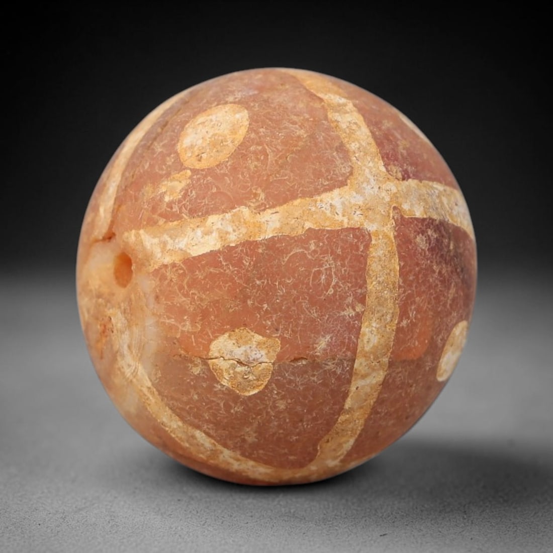Ancient Carnelian Etched Bead - Gandhara Archaeological Find, 19BE: Carved from natural carnelian, the bead is spherical in form, adorned with white etched cross-shaped banding and circular dot motifs across its surface. A lateral drilled suspension hole is present, c