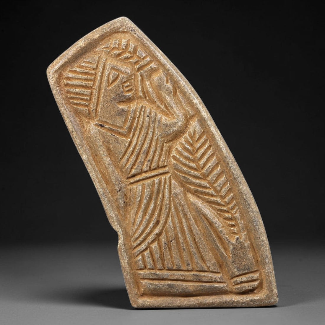 Ancient Stone Plaque Relief - Near Eastern Standing Figure, 73BE: Carved from a single piece of stone, this irregularly shaped relief plaque depicts a standing human figure in the stylized, linear artistic tradition of the ancient Near East. The figure is rendered w