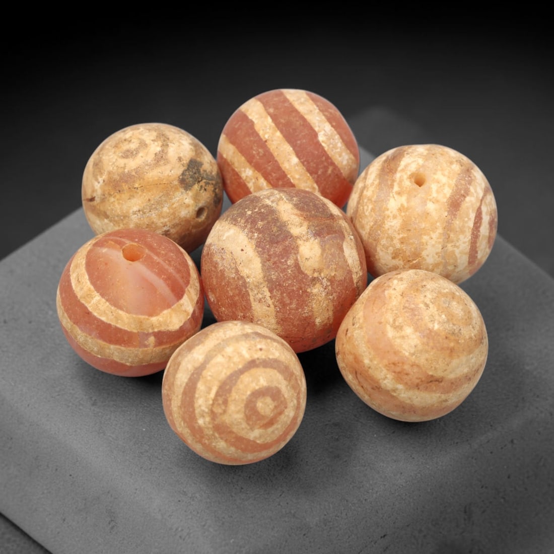 Ancient Carnelian Etched Beads - Gandhara Amulet Set, 73XY: Set of seven spherical beads crafted from carnelian, each decorated with etched concentric and linear geometric motifs in a pale white pigment, characteristic of Gandharan decorative traditions. The b