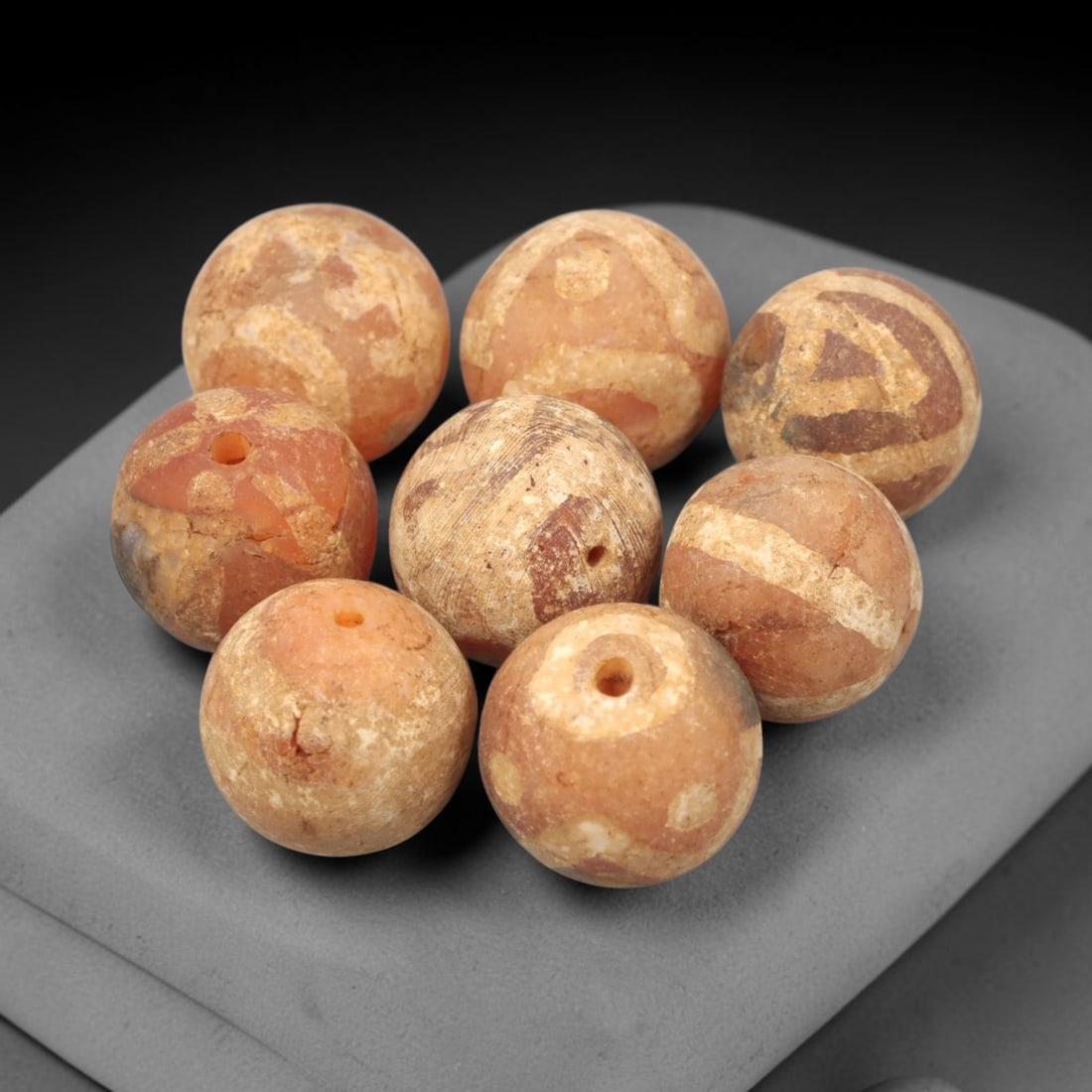 Ancient Carnelian Etched Beads - Gandhara Amulet Set, 70XY: Set of eight spherical beads crafted from carnelian, each decorated with etched geometric motifs in a pale white pigment, characteristic of Gandharan decorative traditions. The beads retain a well-dev