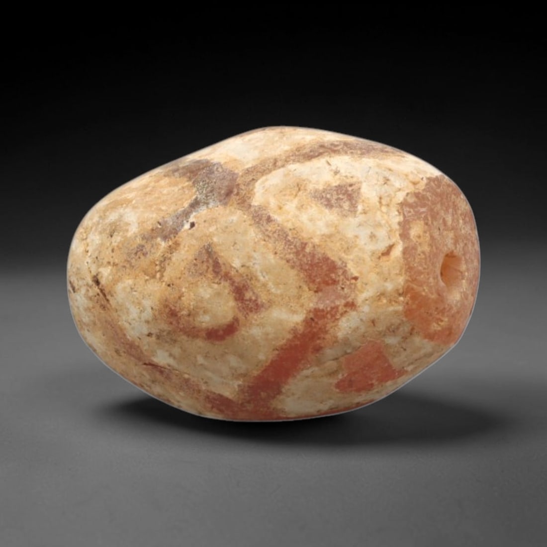 Ancient Carnelian Etched Bead - Gandhara Amulet, 33XY: Carved from carnelian, the bead is fashioned in a rounded oval form with a lateral drilled suspension hole for wear. The surface bears a partial white-etched geometric pattern, characteristic of Gandh