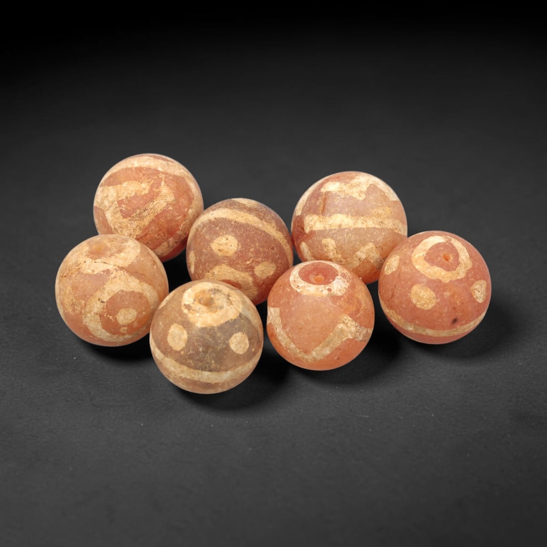 Ancient Carnelian Etched Beads - Gandhara Amulet Set, 79XY: Set of seven spherical beads crafted from carnelian, each decorated with etched circular and geometric motifs in a pale white pigment, characteristic of Gandharan decorative traditions. The beads reta