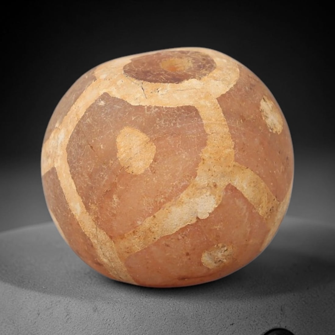 Ancient Carnelian Etched Bead - Gandhara Archaeological Find, 24BE: Carved from natural carnelian, the bead is spherical in form, adorned with white etched geometric motifs including angular bands and circular accents across its surface. A lateral drilled suspension h