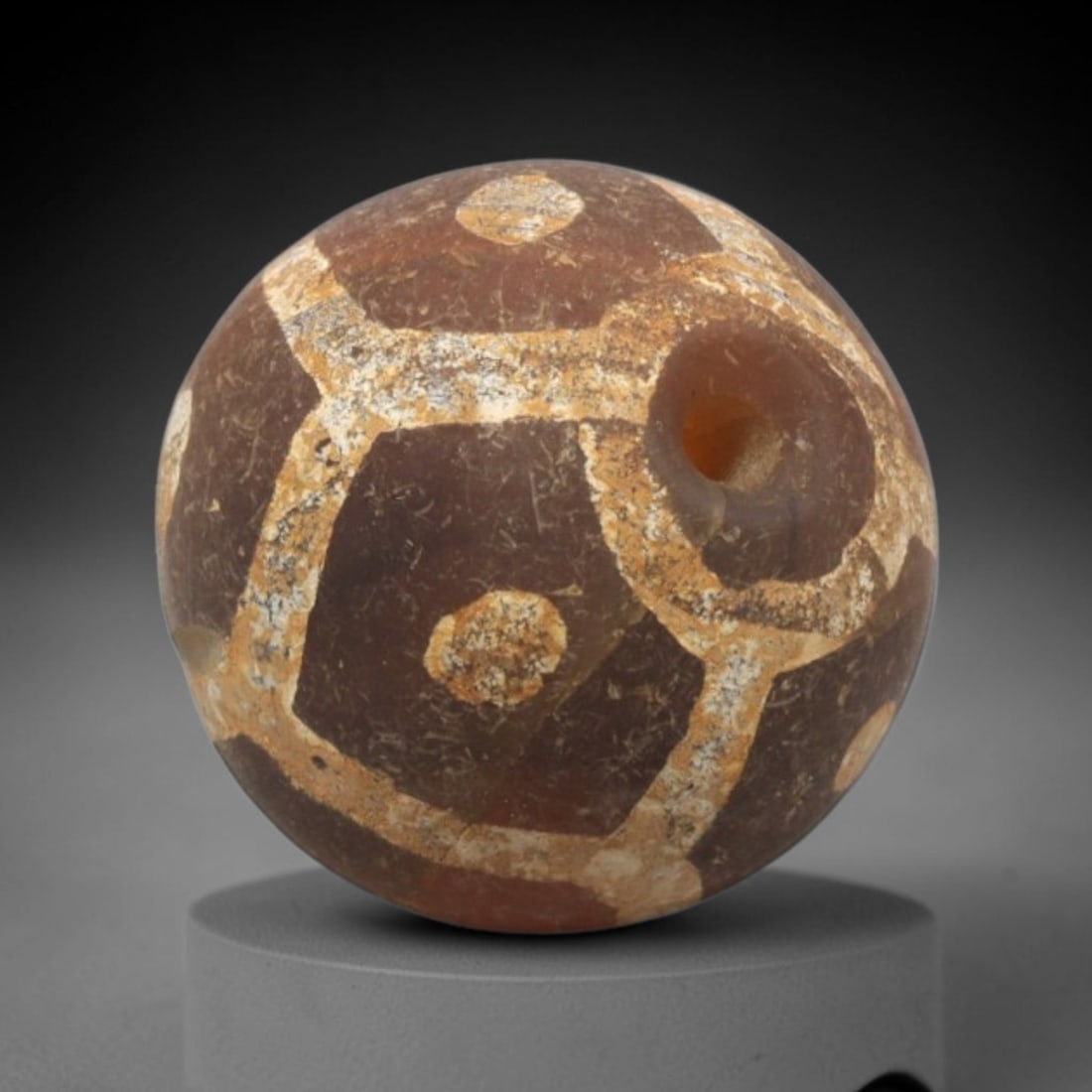 Ancient Carnelian Etched Bead - Gandhara Spherical Bead, 22XY: The bead is fashioned from carnelian, a semi-precious chalcedony, with a spherical form and a laterally drilled suspension hole for wear. Its surface is decorated with an etched white geometric lattic