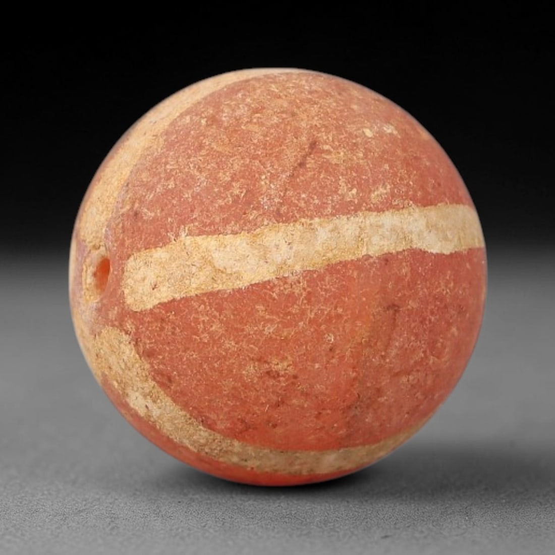 Ancient Carnelian Etched Bead - Gandhara Archaeological Find, 10BE: Carved from natural carnelian, the bead is spherical in form, decorated with white etched linear band motifs across its surface. A lateral drilled suspension hole is present, consistent with Gandharan