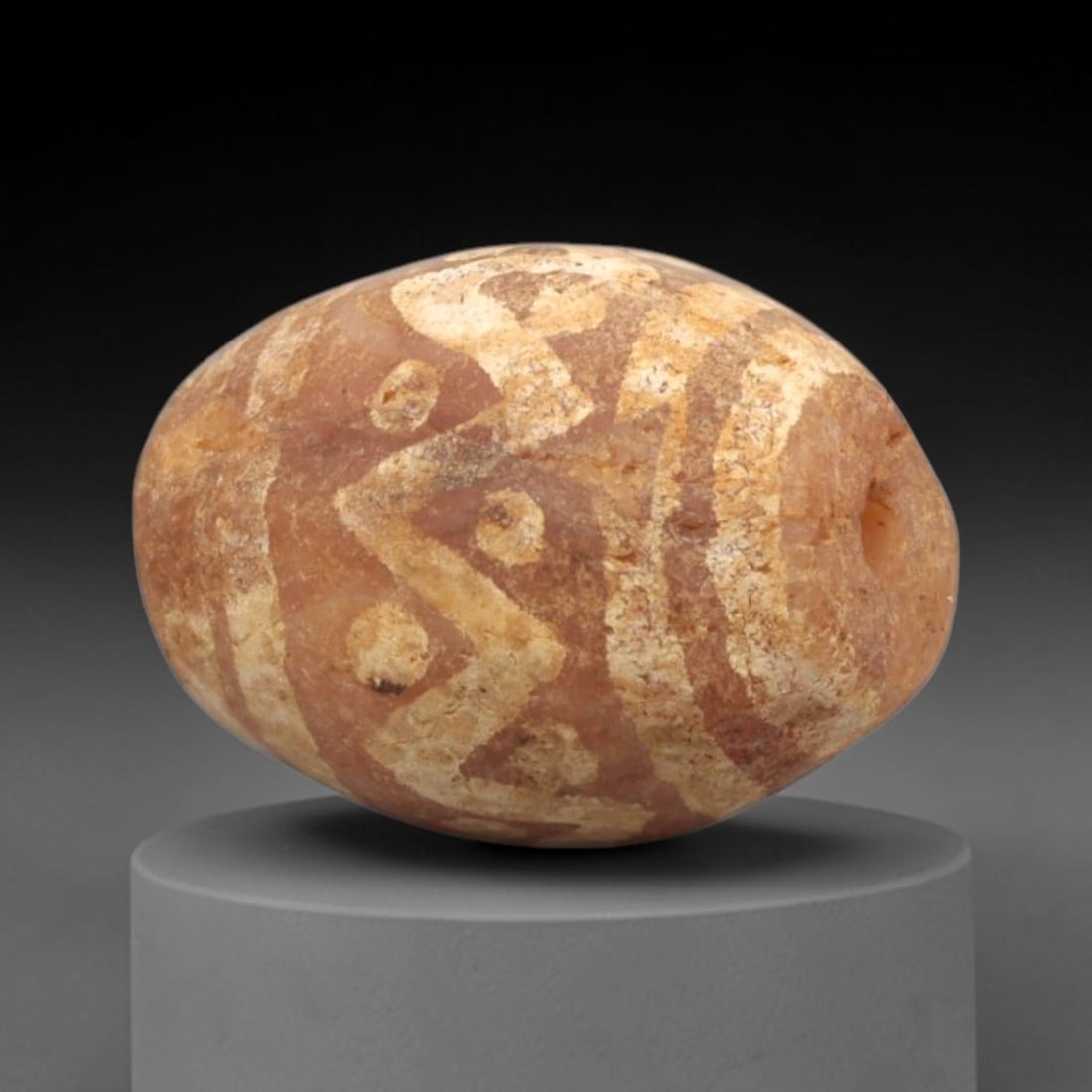 Ancient Carnelian Etched Bead - Gandhara Amulet, 38XY: Carved from carnelian, the bead is fashioned in an oval barrel shape with a lateral drilled suspension hole for wear. The surface is adorned with intricate white-etched geometric motifs, including int