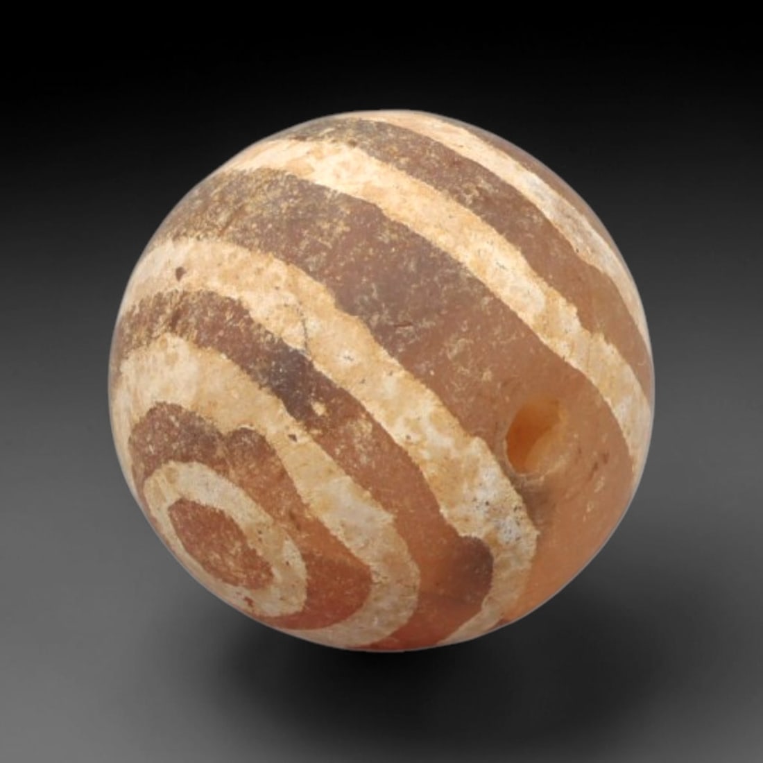 Ancient Carnelian Etched Bead - Gandhara Spherical Bead, 25XY: The bead is fashioned from carnelian, a semi-precious chalcedony, with a spherical form and a laterally drilled suspension hole for wear. Its surface is decorated with an etched white pattern of conce