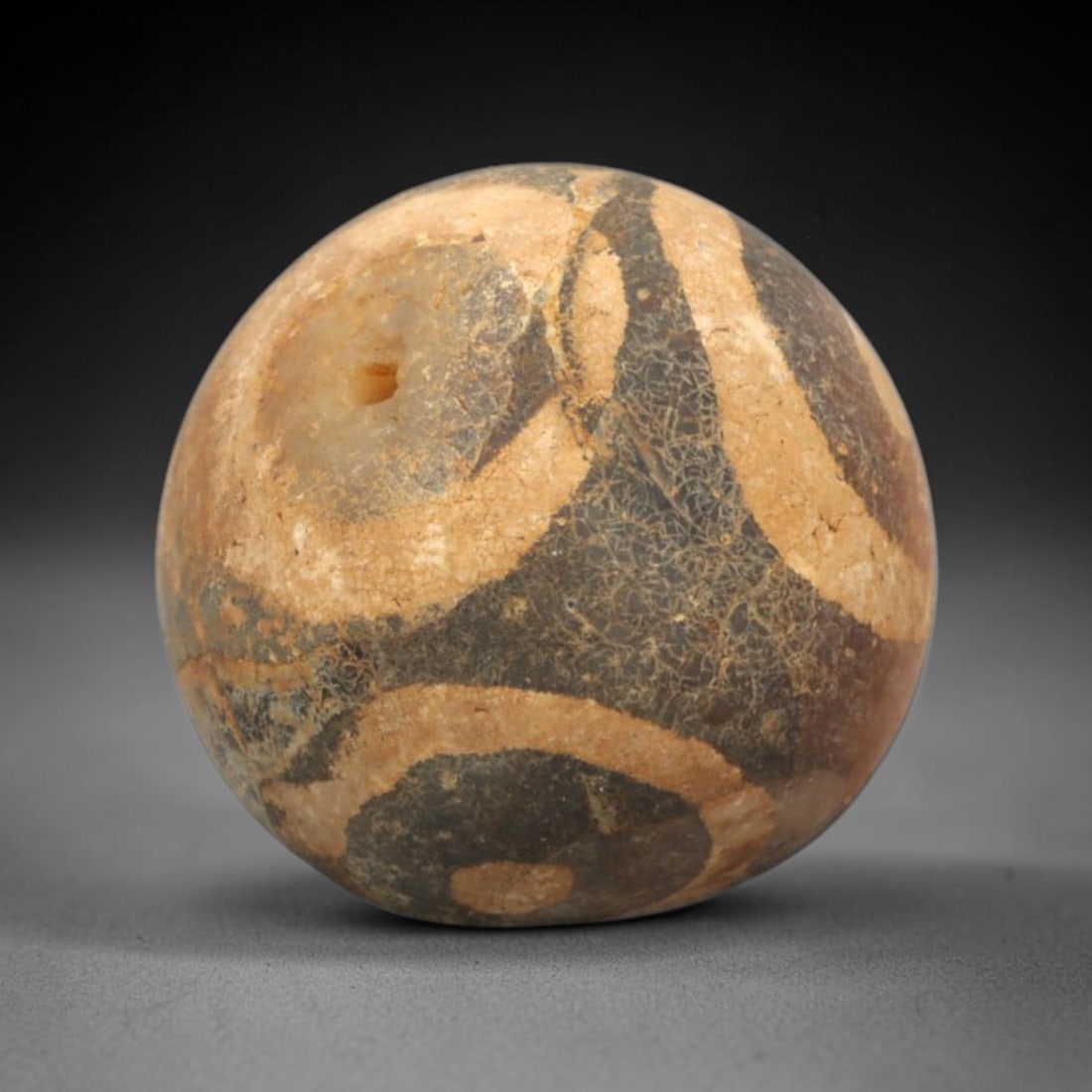 Ancient Carnelian Etched Bead - Gandhara Spherical Bead, 19XY: The bead is carved from carnelian, a semi-precious chalcedony, with a spherical form and a laterally drilled suspension hole. Its surface features an etched white pattern of circular and curved banded