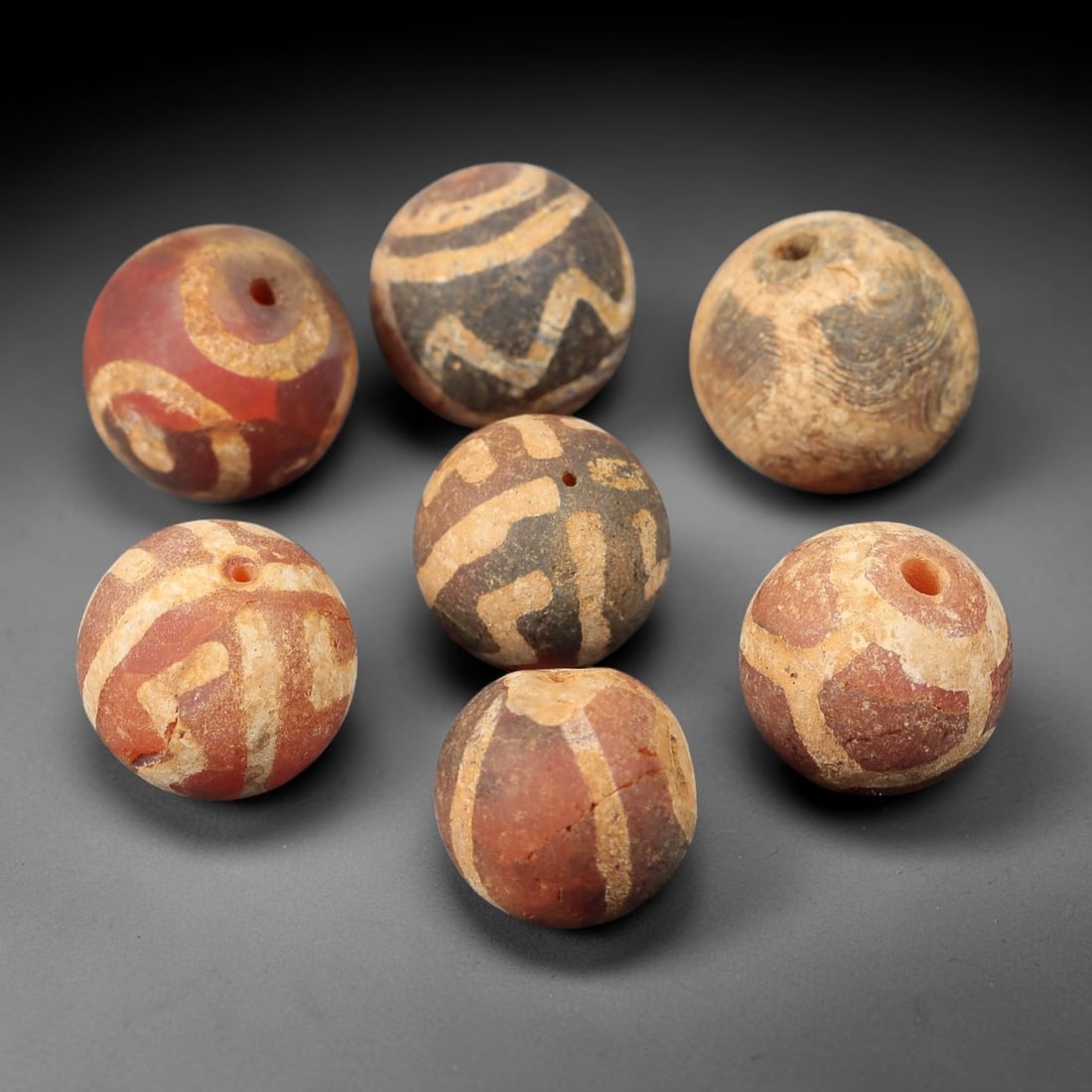 Ancient Carnelian Etched Beads - Gandhara Amulet Set, 42BE: Set of seven spherical beads crafted from carnelian, each decorated with etched geometric motifs in a pale white pigment, characteristic of Gandharan decorative traditions. The beads retain a well-dev
