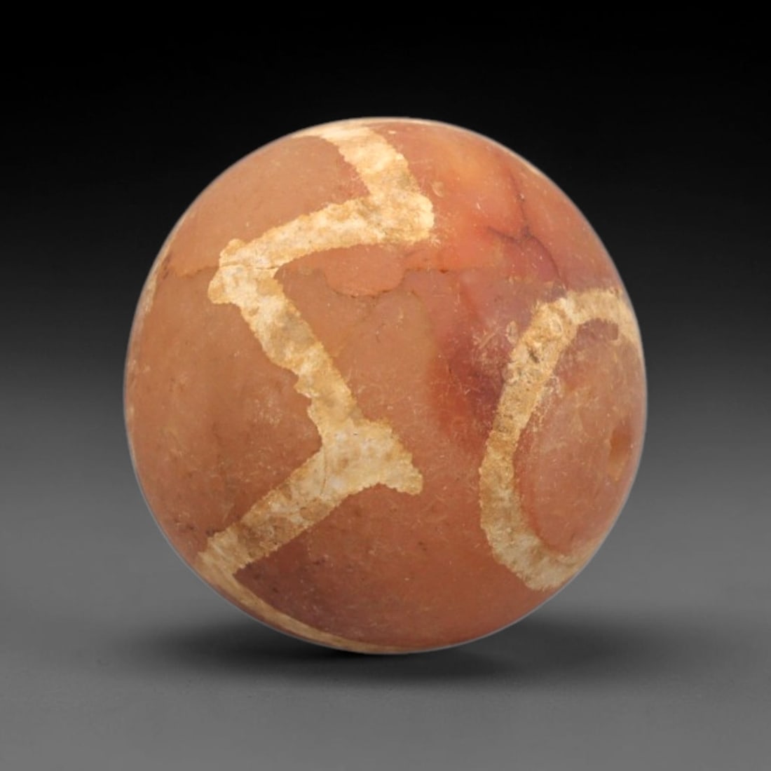 Ancient Carnelian Etched Bead - Gandhara Spherical Bead, 26XY: The bead is crafted from carnelian, a semi-precious chalcedony, with a spherical form and laterally drilled suspension hole. Its surface is decorated with an etched white geometric pattern of angular