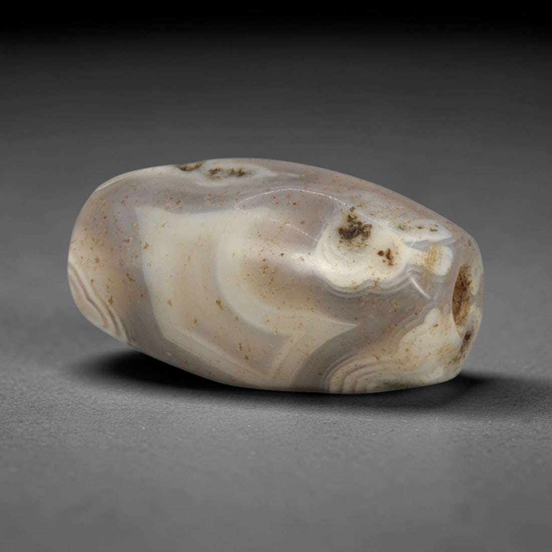 Ancient Agate Bead - Bactrian Faceted Banded Agate Bead, 19XW: This bead is carved from translucent smoky-grey and creamy-white banded agate, shaped into a refined, faceted barrel form with a precisely centered axial drill hole, characteristic of ancient Bactrian