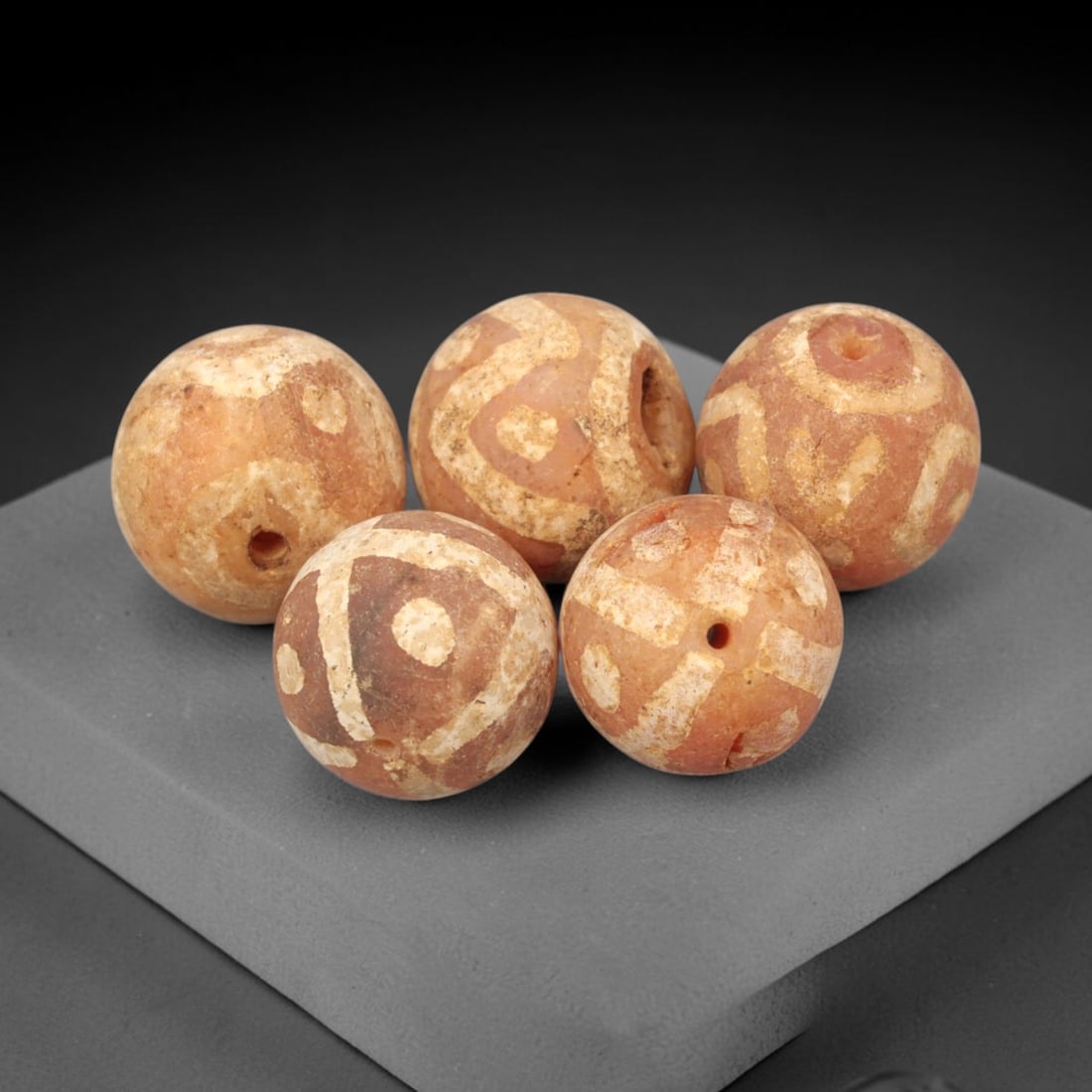 Ancient Carnelian Etched Beads - Gandhara Amulet Set, 62XY: Set of five spherical beads crafted from carnelian, each decorated with etched geometric motifs in a pale white pigment, characteristic of Gandharan decorative traditions. The beads retain a well-deve