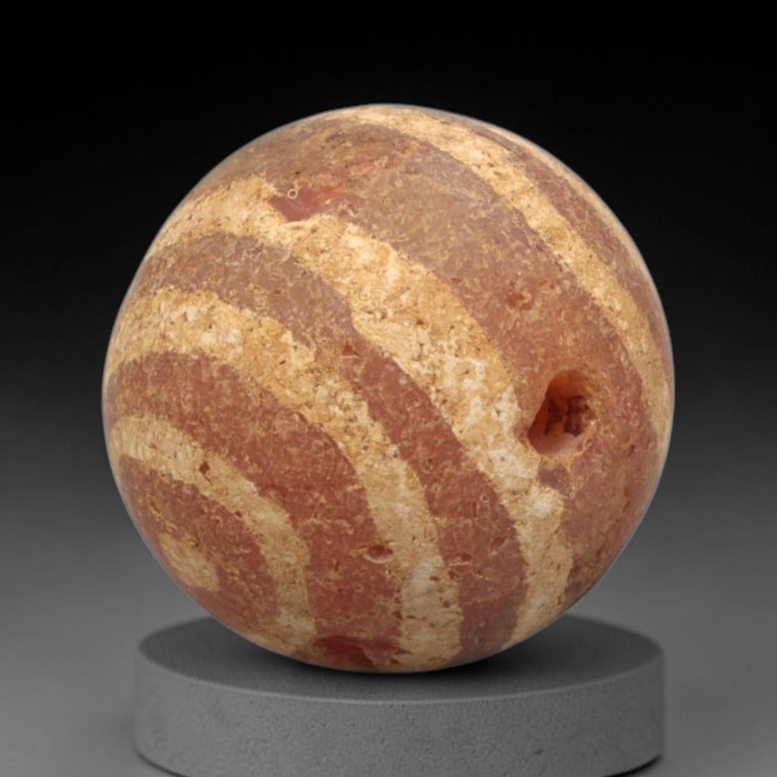 Ancient Carnelian Etched Bead - Gandhara Spherical Bead, 17XY: The bead is fashioned from carnelian, a semi-precious chalcedony, with a spherical form and a laterally drilled suspension hole for wear. Its surface is decorated with an etched white pattern of sweep