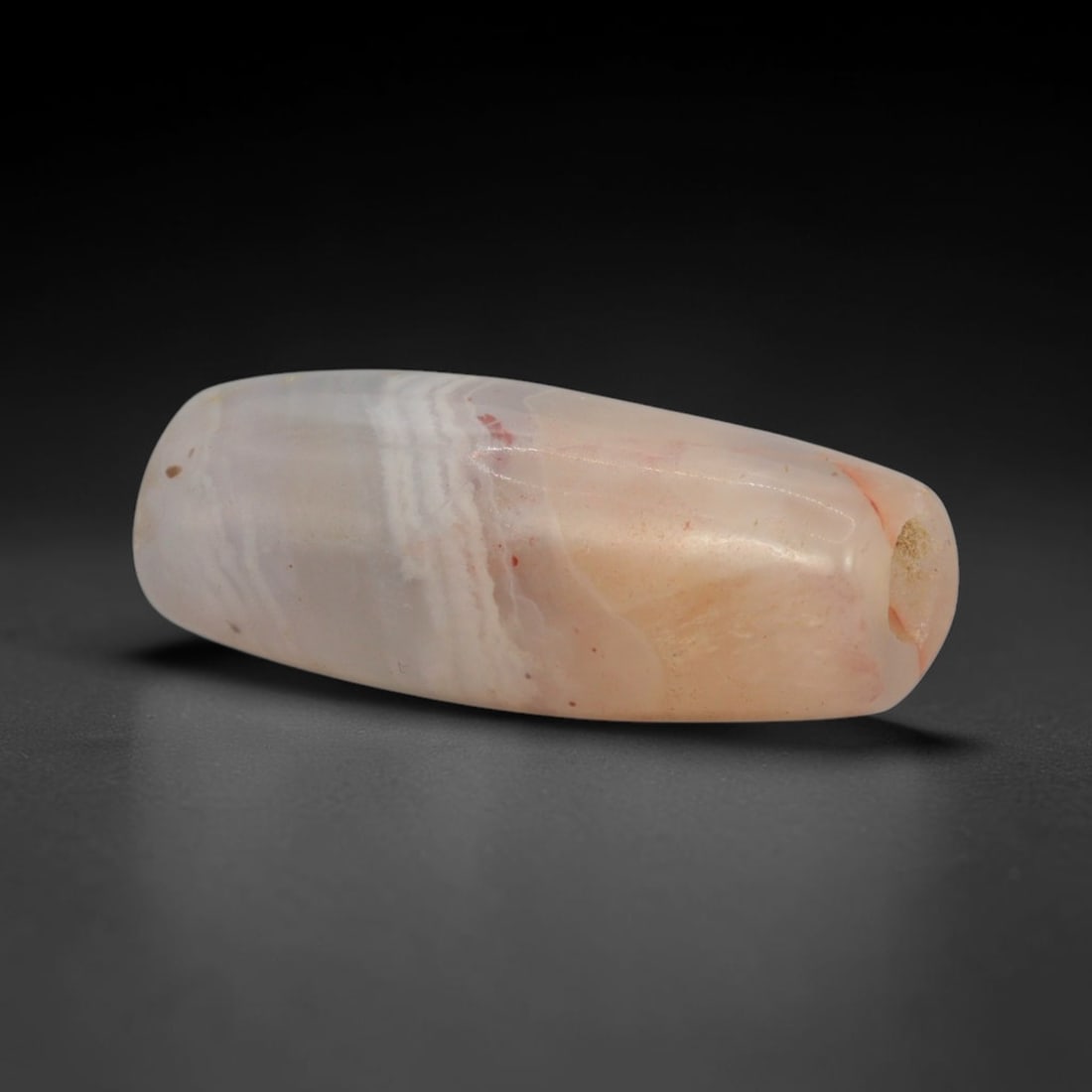 Ancient Agate Bead - Bactrian Banded Barrel Bead, 22XW: This bead is fashioned from translucent pale peach-agate with contrasting creamy-white wavy banding, shaped into a refined elongated barrel form with a precisely centered axial drill hole, characteris