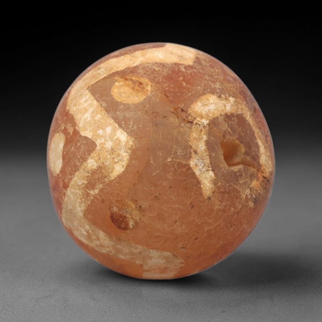 Ancient Carnelian Etched Bead - Gandhara Spherical Bead, 15XY: The bead is crafted from carnelian, a semi-precious chalcedony, with a spherical form and laterally drilled suspension hole. Its surface features an etched white pattern of angular bands and circular