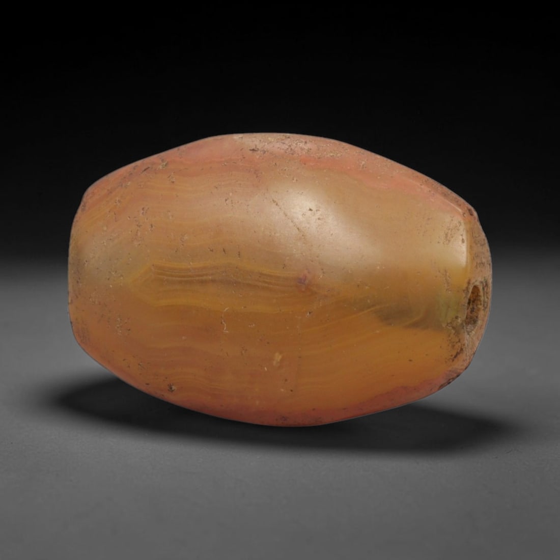 Ancient Agate Bead - Bactrian Carnelian Banded Barrel Bead, 7XW: This bead is carved from translucent honey-amber and warm pinkish-red banded carnelian agate, shaped into a smooth, robust barrel form with a precisely centered axial drill hole, characteristic of anc