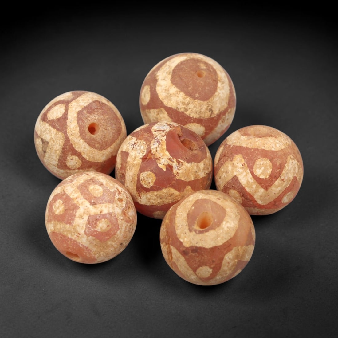 Ancient Carnelian Etched Beads - Gandhara Amulet Set, 61XY: Set of six spherical beads crafted from carnelian, each decorated with etched circular and geometric motifs in a pale white pigment, characteristic of Gandharan decorative traditions. The beads retain