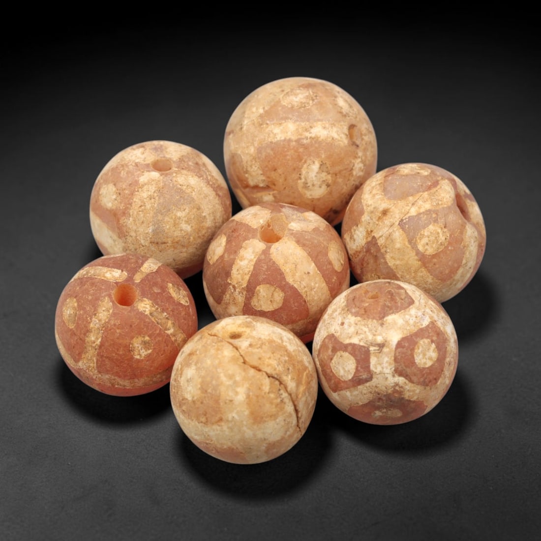 Ancient Carnelian Etched Beads - Gandhara Amulet Set, 66XY: Set of seven spherical beads crafted from carnelian, each decorated with etched geometric motifs in a pale white pigment, characteristic of Gandharan decorative traditions. The beads retain a well-dev