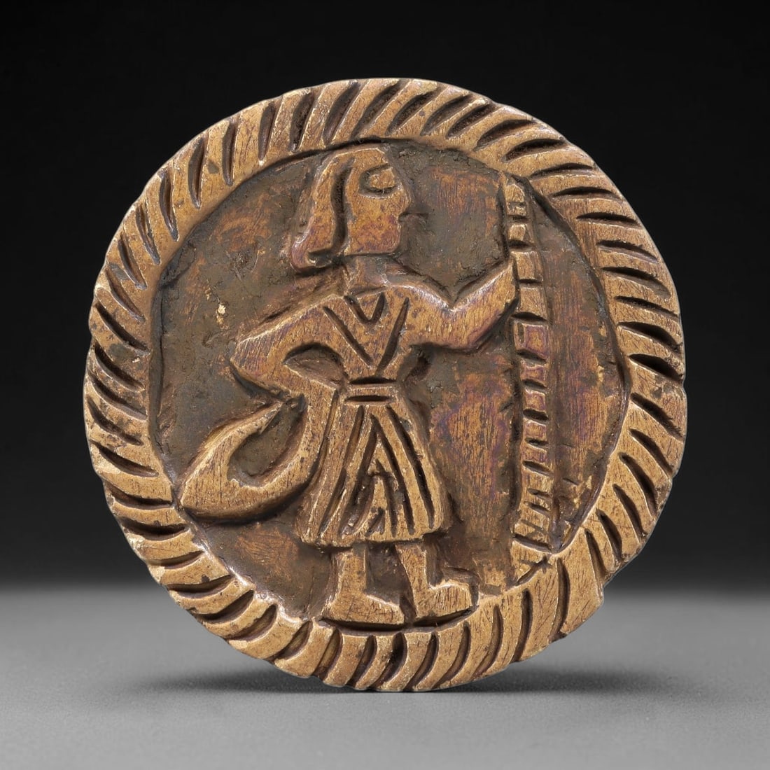 Ancient Steatite Plaque - Near Eastern Standing Figure Relief, 94BE: Carved from steatite, the circular plaque features a raised relief of a standing human figure, rendered with incised linear details defining a V-neck tunic, a patterned waistband, and a pleated skirt.