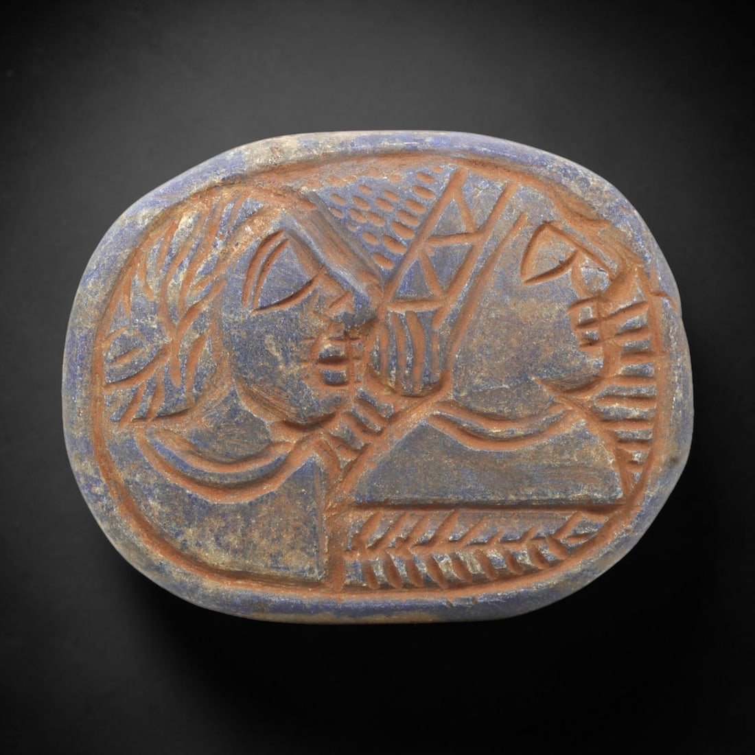 Near Eastern Lapis Lazuli Plaque - Tribal Art Two Figure Relief, 95ZY: Carved from lapis lazuli, this oval plaque features a deeply incised relief composition depicting two facing stylized human figures, rendered in a geometric Near Eastern tribal idiom. A central geomet