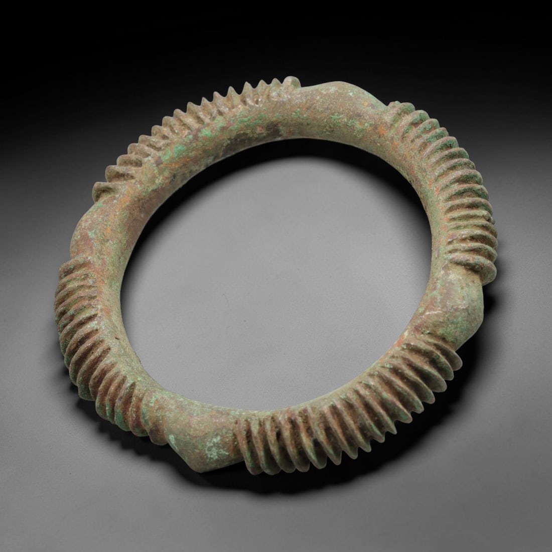 A European Bronze Ribbed Bracelet, 8th-10th Century, 95FT: Cast from bronze with a thick, rounded section, the bracelet is formed as a near-complete circle with four distinct, raised, angular nodes evenly spaced around its circumference. Between each node, th
