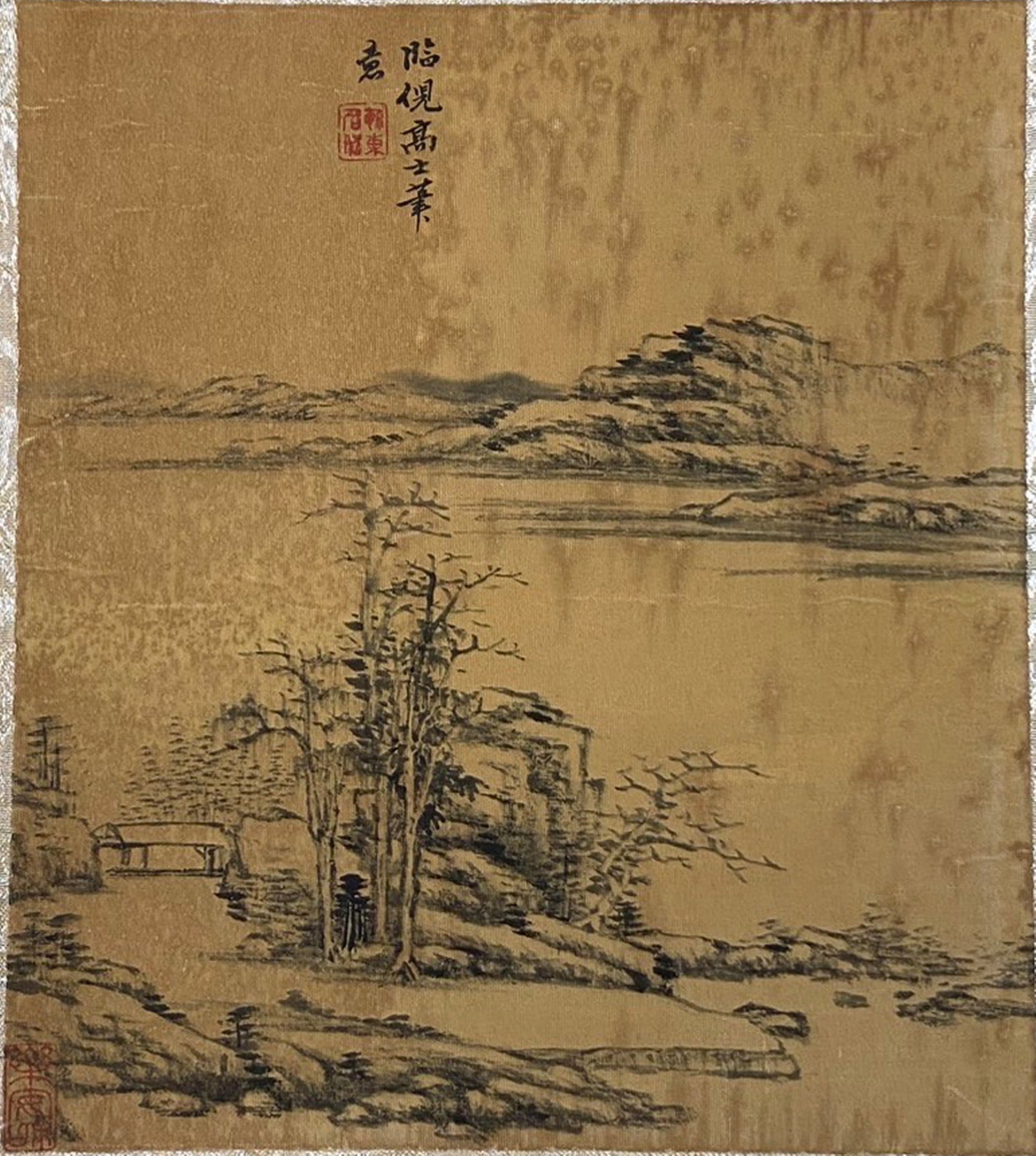 A Chinese Ink and Color Textile Print, After Ni Zan's 'Wintry Trees by a Lake', 20th Century, 40FK: Printed on woven silk or hemp textile with a gold-toned ground, the composition follows the sparse, reductive style of Yuan Dynasty painter Ni Zan. Bare, angular trees stand beside a quiet lake, with