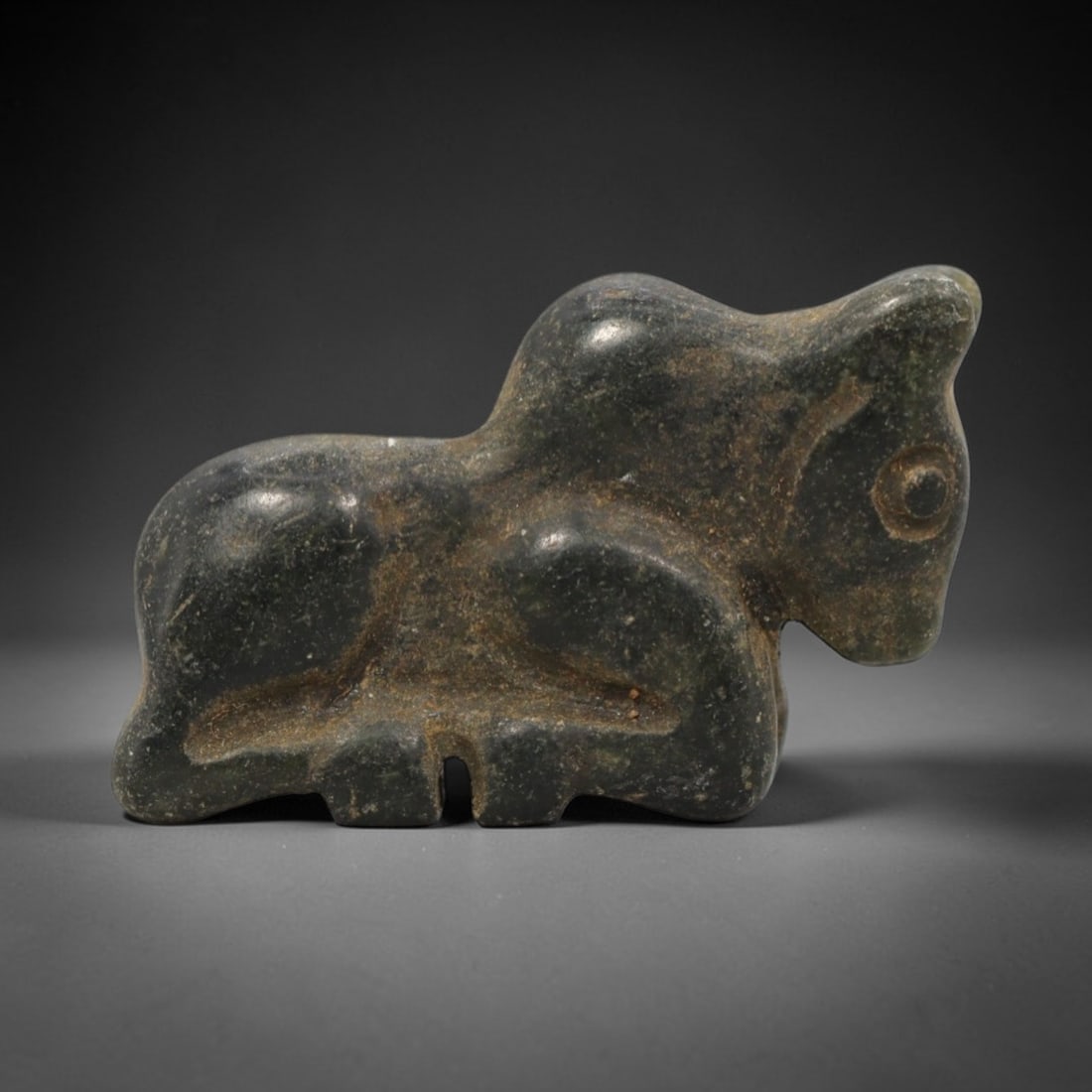 Ancient Near Eastern Green Stone Bull Amulet - Carved Figurine, 84ZW: This amulet is carved from a dense, dark green stone, likely serpentine or steatite, with subtle incised details defining its recumbent bull form. The piece depicts a bull in a resting pose, with dist