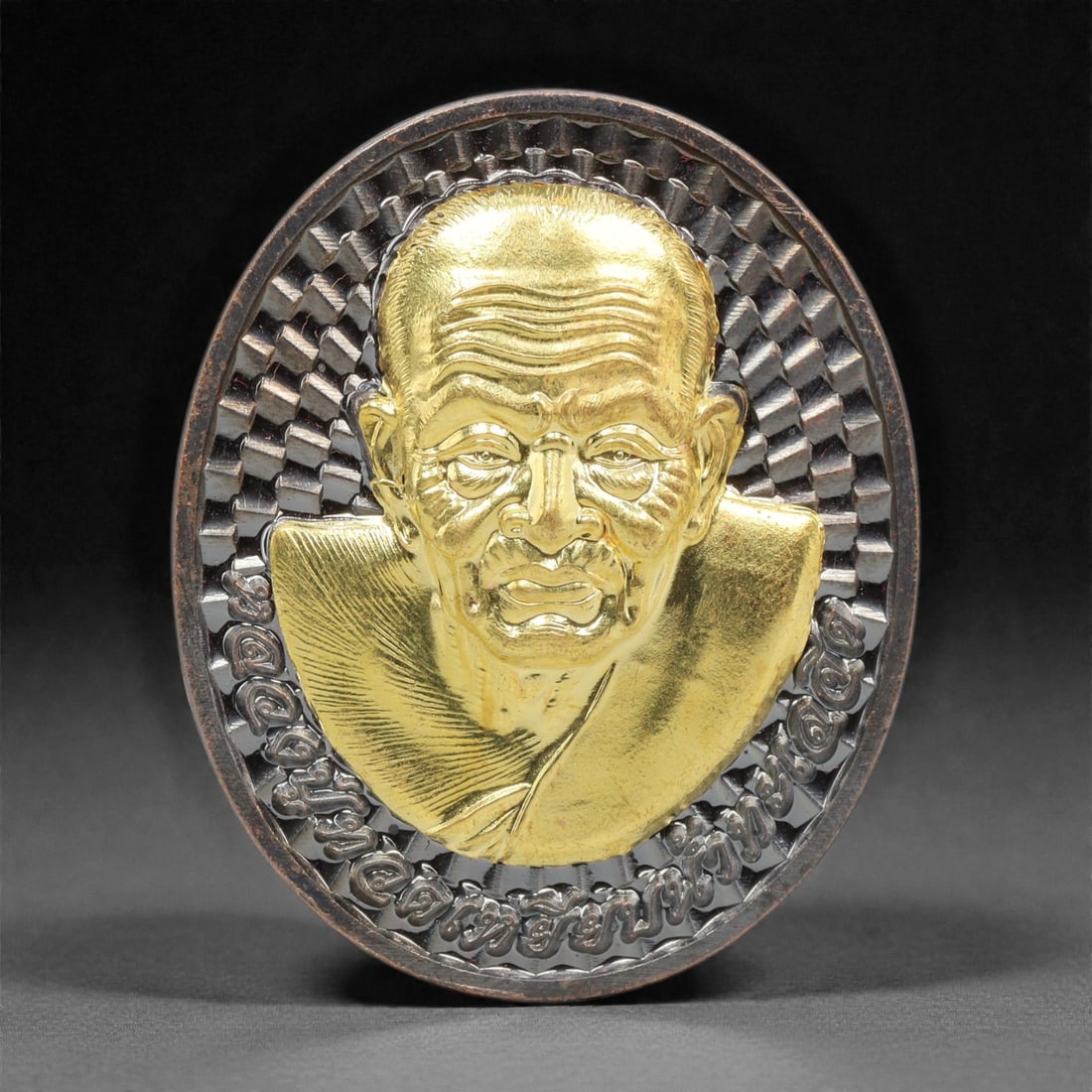 A Thai Bi-Metallic Monk Portrait Medallion, 21st Century, 92FP: Cast with a bi-metallic construction, the medallion is oval and double-sided with a raised dark metal border. The obverse features a high-relief bust portrait of a Buddhist monk rendered in gilt metal