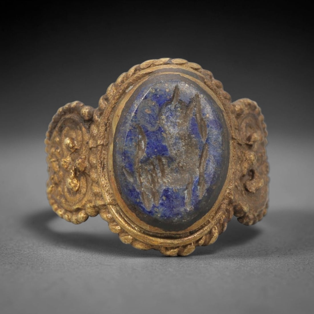 Antique Qajar Dynasty Brass Lapis Lazuli Intaglio Ring - Size 9 US, 13WJ: This antique Qajar dynasty brass intaglio ring features an oval lapis lazuli intaglio inset with incised figural carvings, set within an ornate brass mount adorned with a beaded border and elaborate d