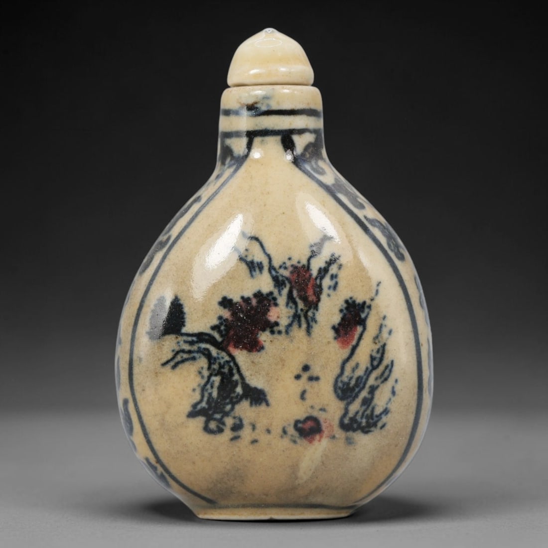 A Chinese Porcelain Snuff Bottle, 20th Century, 3YD: Crafted from porcelain with a pale cream glaze and decorated in underglaze blue with copper red accents, the snuff bottle features a flattened, pear-shaped body, a short cylindrical neck, and a domed