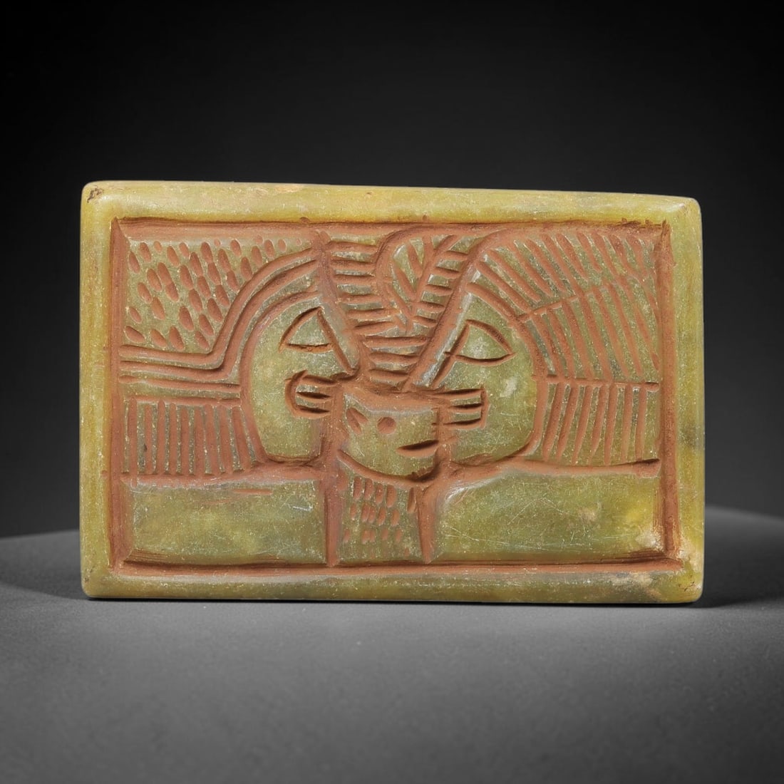 Near Eastern Serpentine Plaque - Tribal Art Two Figure Relief, 54BF: Carved from serpentine, this rectangular plaque features a deeply incised relief composition centered on two stylized human faces flanking a central zoomorphic or symbolic motif. The figures are rende
