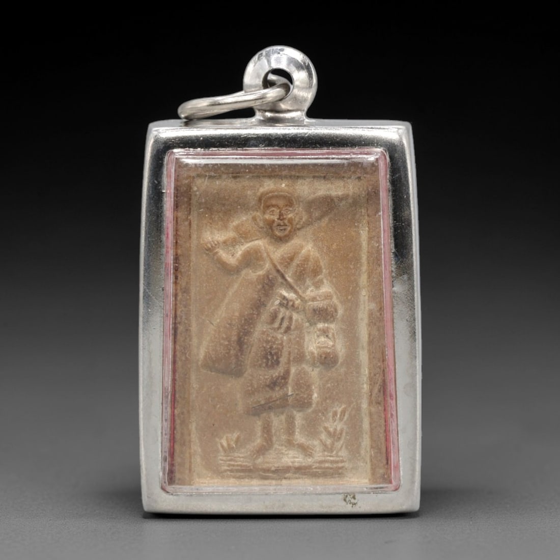 A Thai Clay Amulet of Thao Wessuwan (Vessavana) in Silver-Tone Case, 20th Century, 10ZK: Rectangular in form, this sacred clay amulet is housed in a polished silver-tone metal case with a red enameled border and a fixed suspension loop at the apex for wear. The obverse features a bas-reli