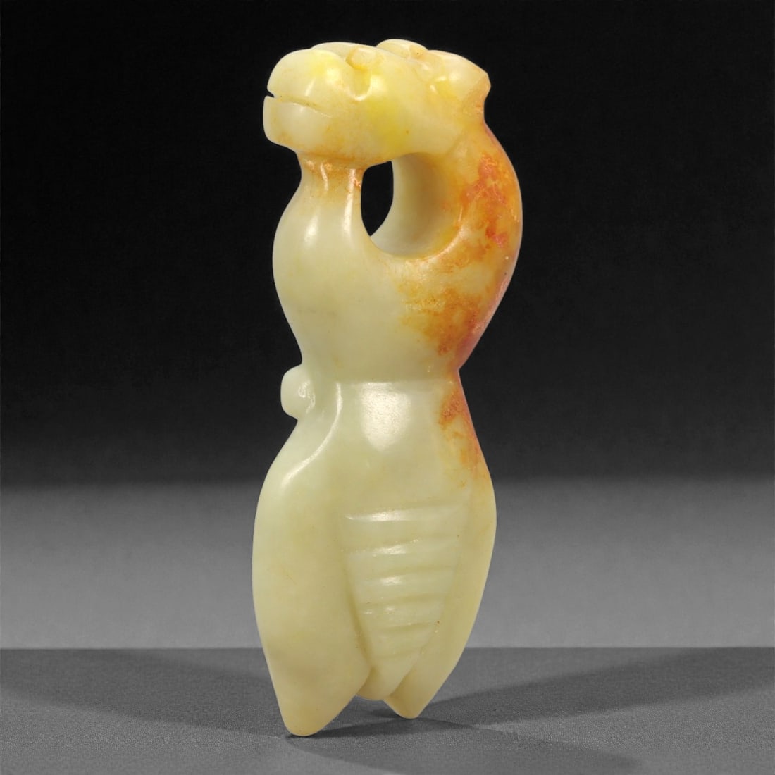 A Chinese Hetian Jade Zoomorphic Carving, 20th Century, 62FH: Carved from pale celadon Hetian nephrite jade with areas of natural russet coloration concentrated along one side, the carving is worked as a compact zoomorphic form with a strongly curved silhouette.