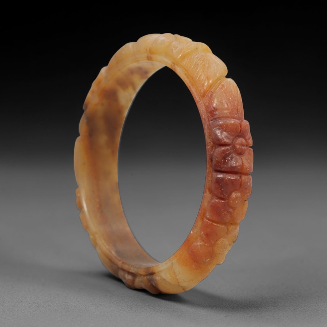A Chinese Carved Jadeite Jade Bangle Bracelet, 20th Century, 43ZL: A fine jadeite bangle of flattened circular form, masterfully carved in relief with a continuous band of floral blossoms and scrolling foliate motifs. The stone exhibits a striking variegated palette,