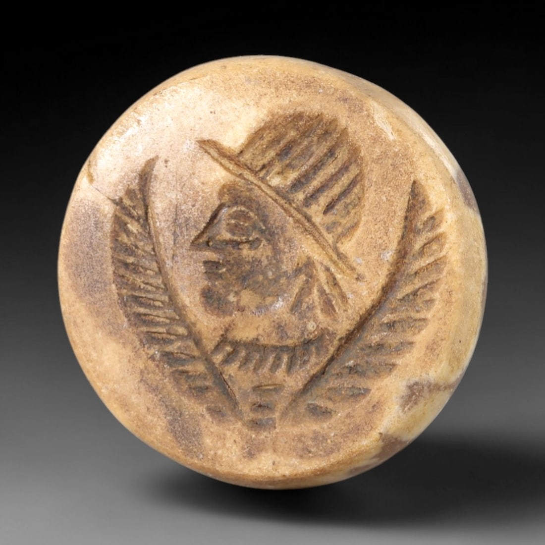 Ancient Stone Profile Bust Intaglio - Near Eastern Amulet, 73AR: This circular intaglio is carved from a pale, creamy stone matrix, featuring a high-relief profile depiction of a human figure, adorned with a feathered headdress and flanked by two stylized palm fron