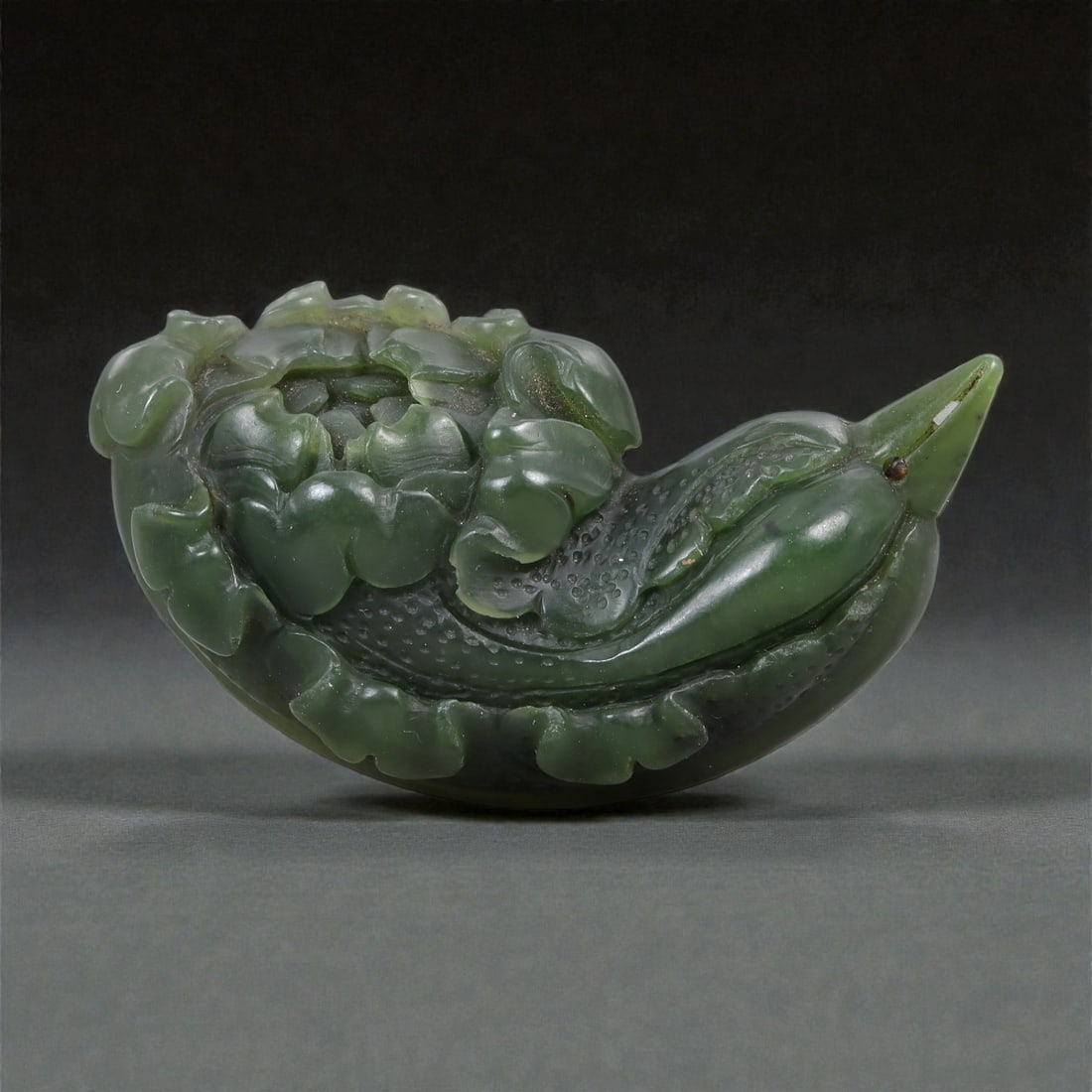 A Chinese Nephrite Jade Flower-Form Ornament, 20th Century, 31FA: Carved from dark green nephrite jade with lighter translucent areas and natural inclusions, the object is worked in the form of a flowering plant shown in low relief. The composition is horizontally o