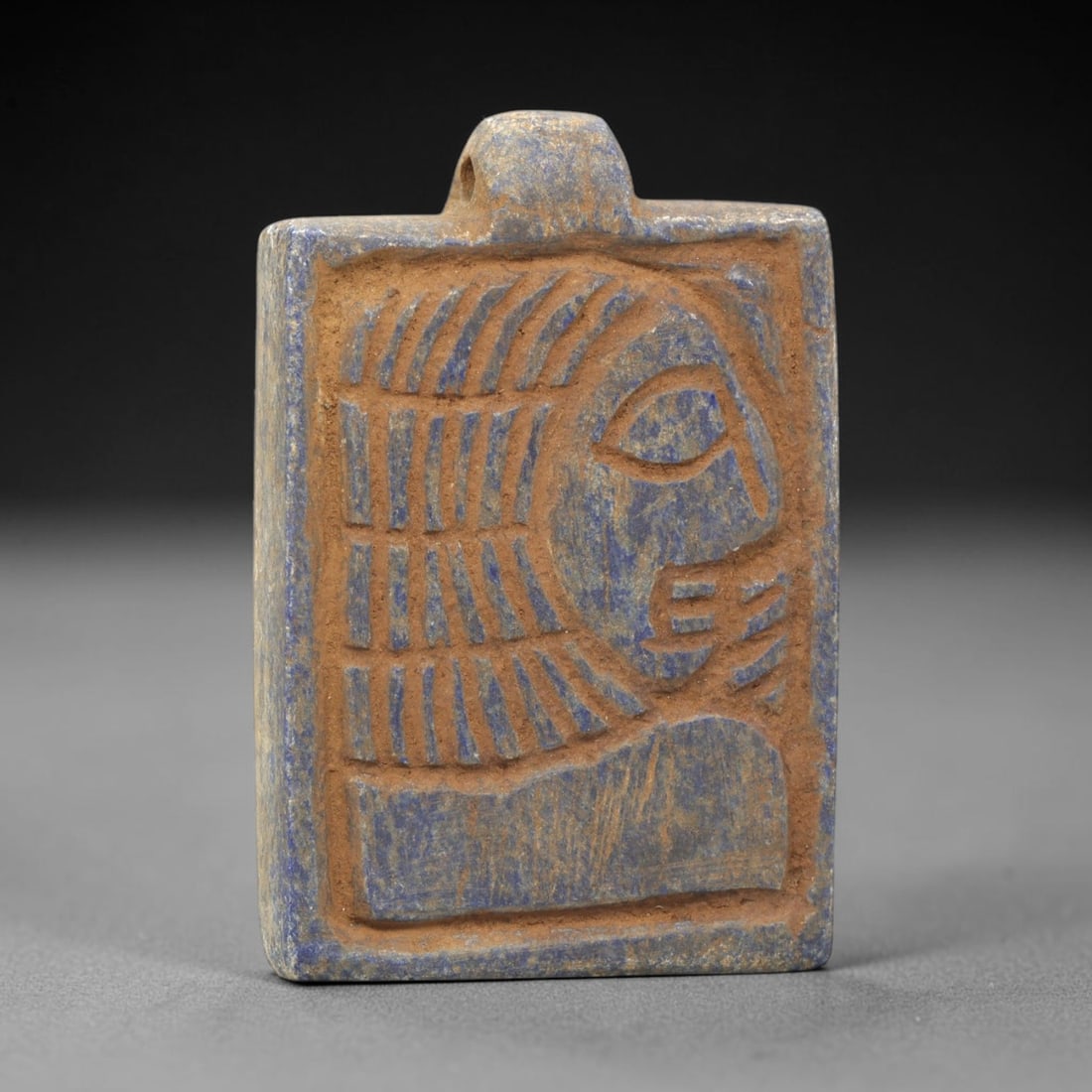 Near Eastern Lapis Lazuli Amulet - Tribal Art Figure Relief Pendant, 53ZY: Carved from lapis lazuli, this rectangular amulet features a deeply incised relief profile of a stylized human figure, rendered in a geometric tribal idiom. The figure is depicted with linear detailin