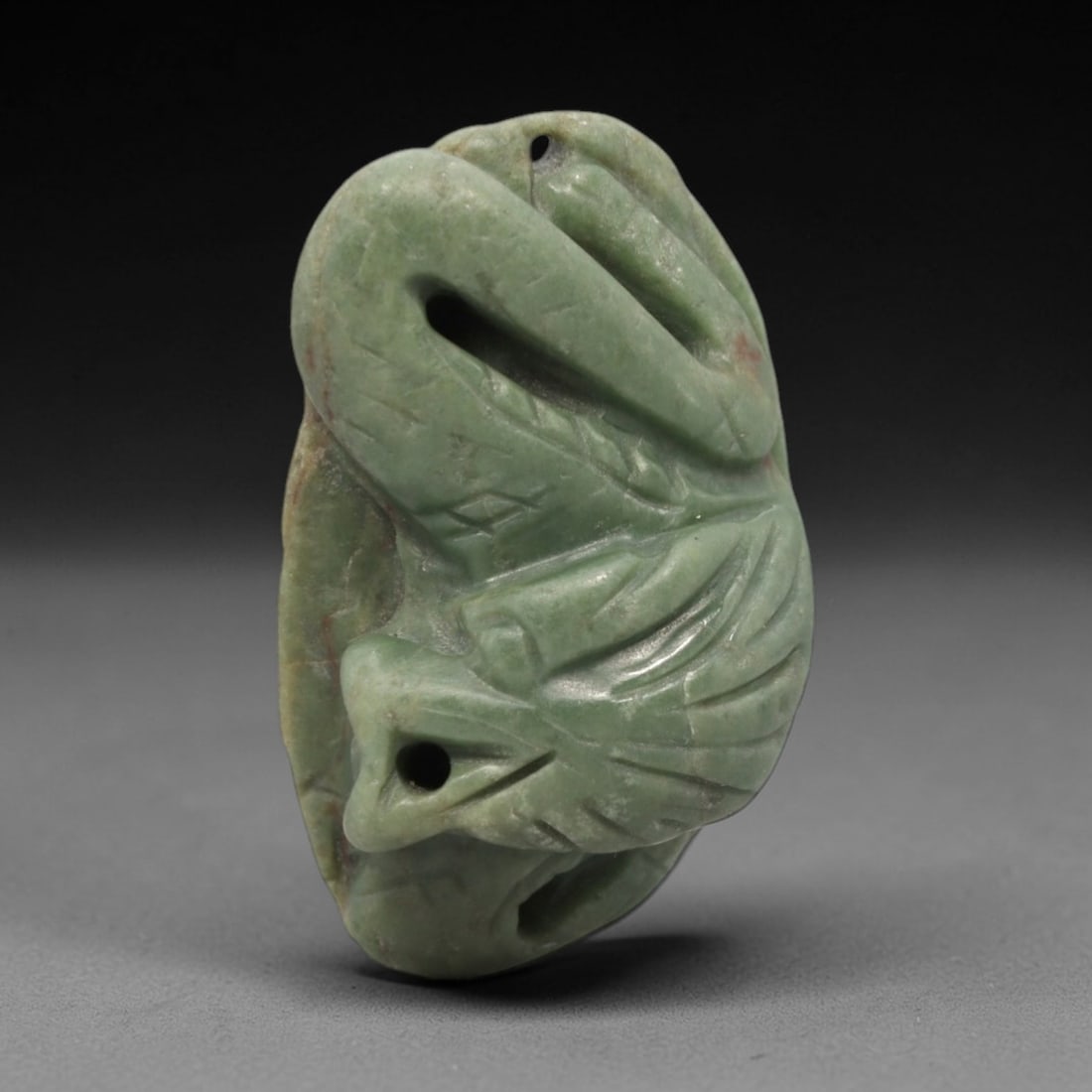 A Chinese Jadeite Jade Dragon-Form Pendant Plaque, 20th Century, 44FR: Carved from uniform celadon jadeite jade with subtle reddish-brown inclusions and a matte finish, the pendant is formed as an irregularly shaped, flattened plaque. The surface is executed in high reli